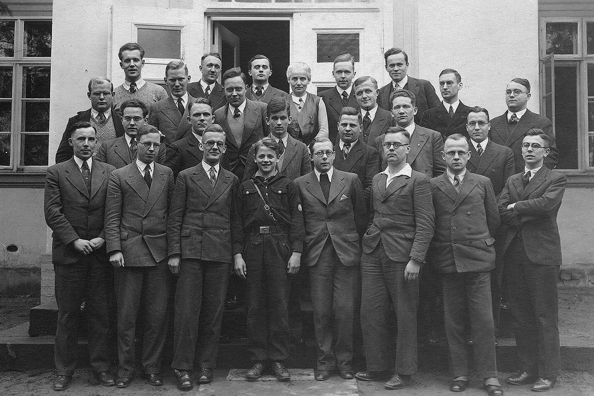 A black-and-white group photograph of seminarians and pastors standing outside a large house, taken at the Confessing Church's underground seminary at Sigurdshof, where Dietrich Bonhoeffer trained ordinands; Bonhoeffer is among those pictured.