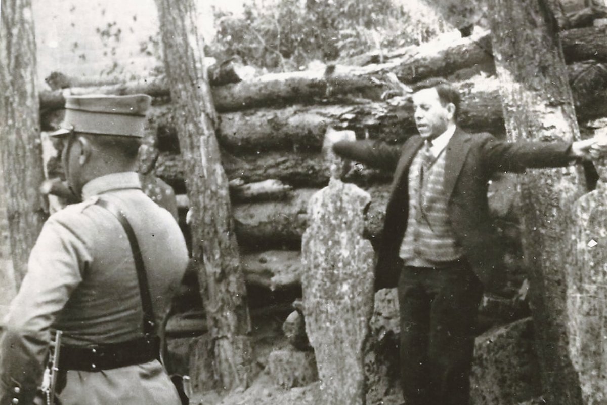 A black-and-white photograph of Miguel Pro standing before a firing squad with his arms spread wide in the shape of a cross, a soldier looking on in the foreground.