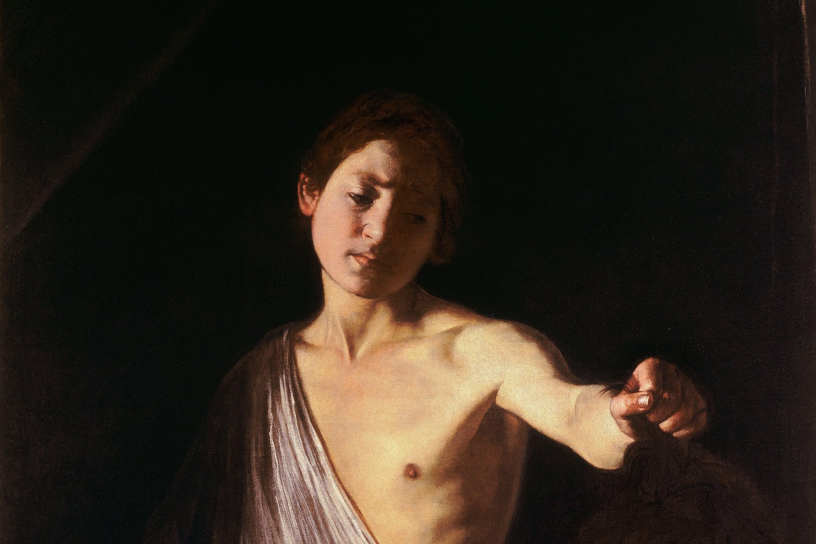 A dramatic Baroque painting of a young man holding a severed head by the hair, his expression sorrowful rather than triumphant, set against a plain dark background.