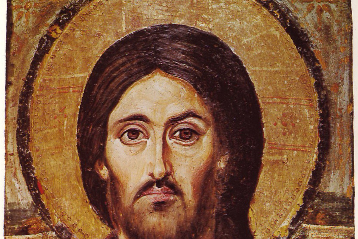 Un'antica icona consumata dal tempo raffigurante Cristo con un'aureola dorata e capelli scuri, l'espressione asimmetrica tra i due lati del volto.