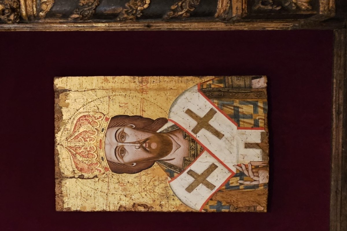 A weathered Byzantine icon of Christ crowned and wearing ornate bishop's vestments marked with large crosses, set within an elaborate gold frame.