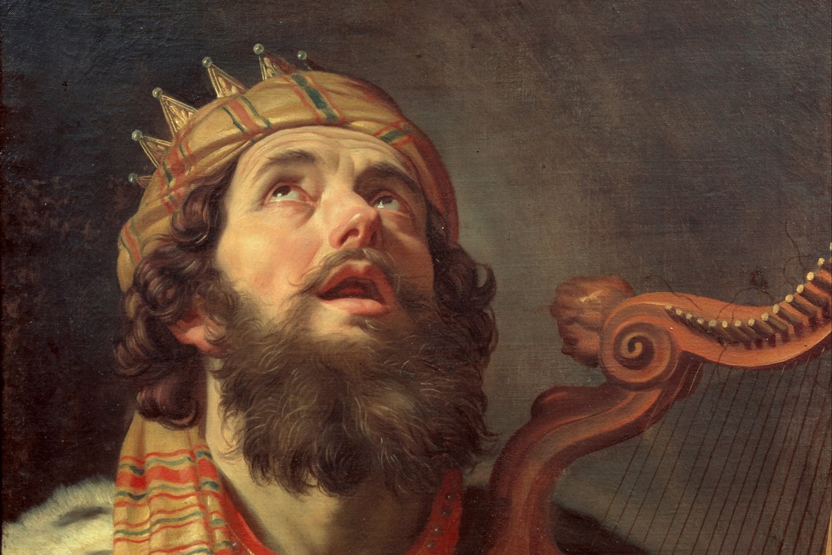 A close-up portrait of a bearded king wearing a jeweled crown, looking upward while playing a harp.