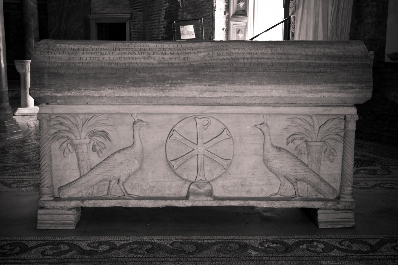 A carved marble sarcophagus panel showing two peacocks flanking a fountain, a common early Christian symbol of resurrection and eternal life.