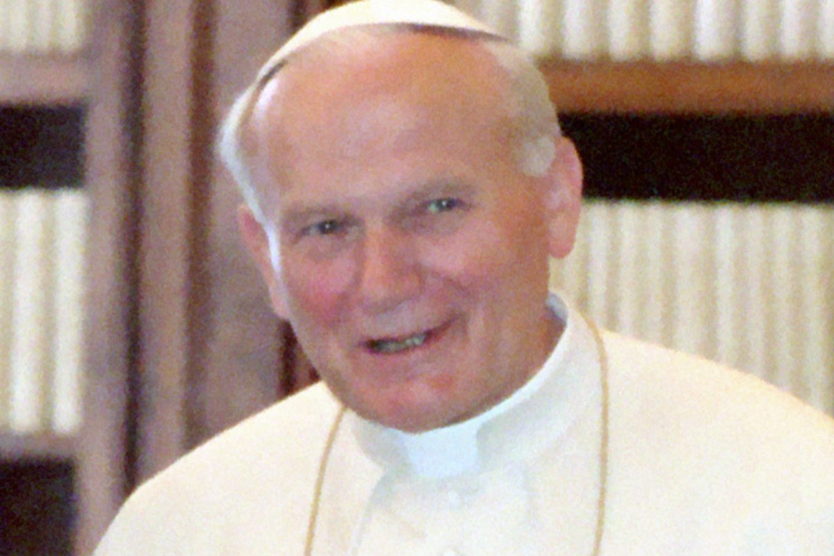 A photograph of an elderly man in white papal vestments, smiling broadly at the camera.