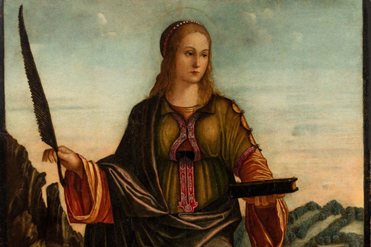A haloed woman in a green robe and red cloak holds a martyr's palm frond and a book, standing before a hillside landscape, in a Renaissance panel painting.