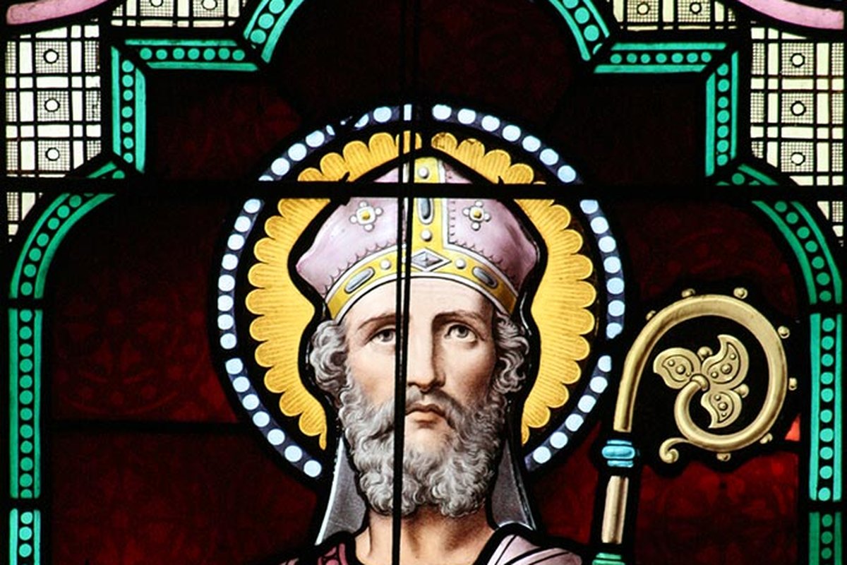 A stained-glass window depicting Saint Anselm of Canterbury as a bishop in green and pink vestments and a mitre, holding a crozier and raising two fingers in blessing, inscribed "St Anselm."