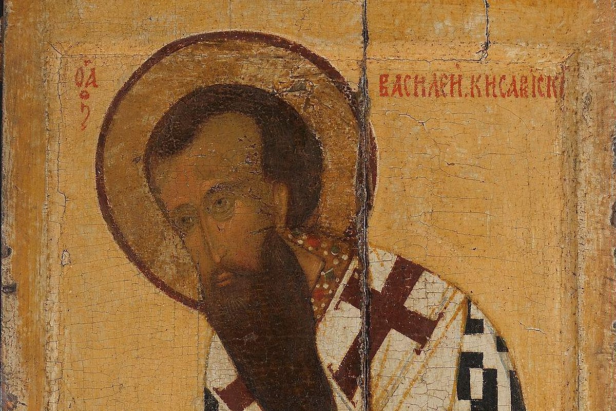 A weathered Russian icon panel of a bearded bishop saint with a golden halo, wearing a white and dark-red cross-patterned omophorion, identified by a Cyrillic inscription as Basil of Caesarea.