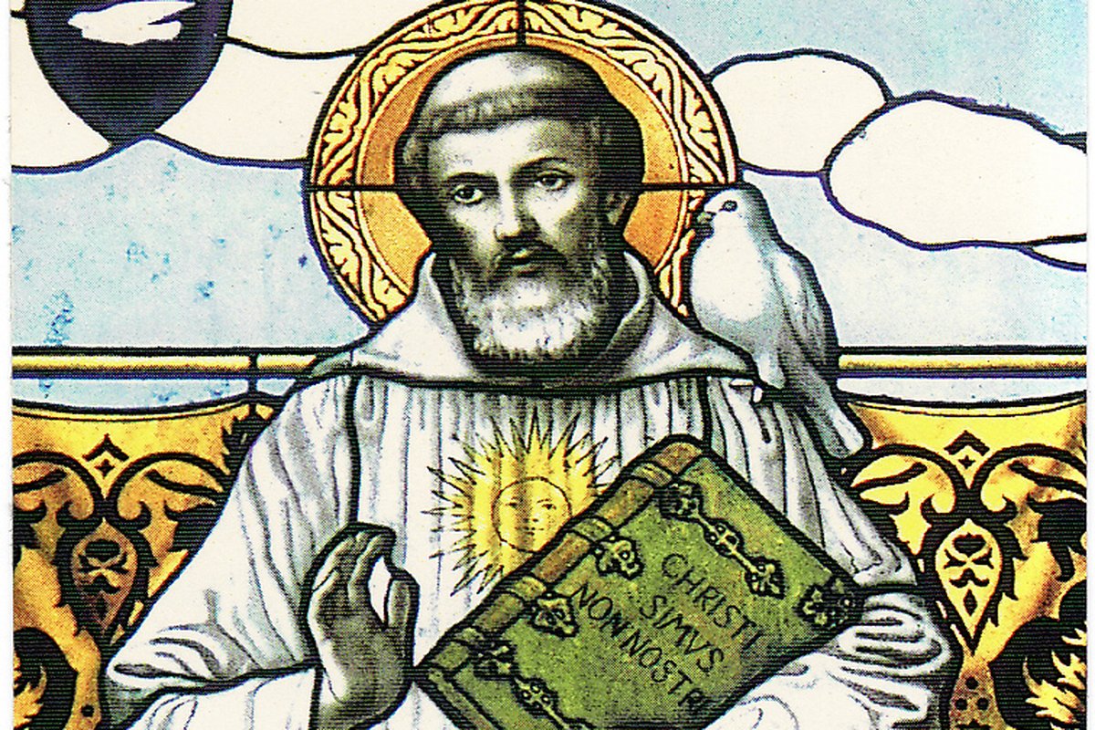 A 19th-century stained-glass window at the Abbey of Bobbio depicting Saint Columban haloed, in a white monk's habit, holding a book inscribed "Christi simus non nostri" with a dove resting near his shoulder.