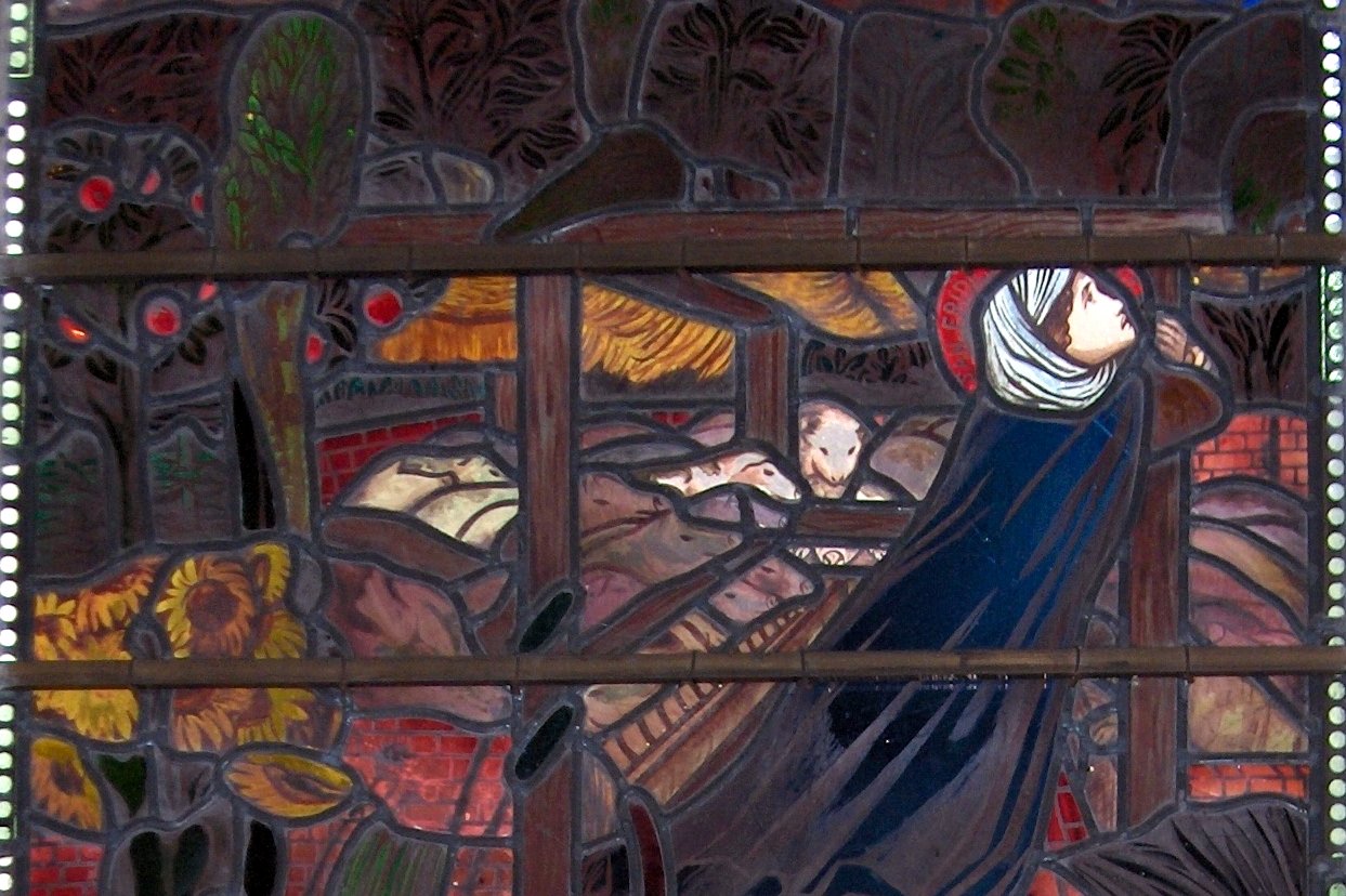 Un vitrail préraphaélite représentant une jeune sainte en habit médiéval entourée de scènes narratives tirées de sa légende, dans des bleus et des rouges profonds.