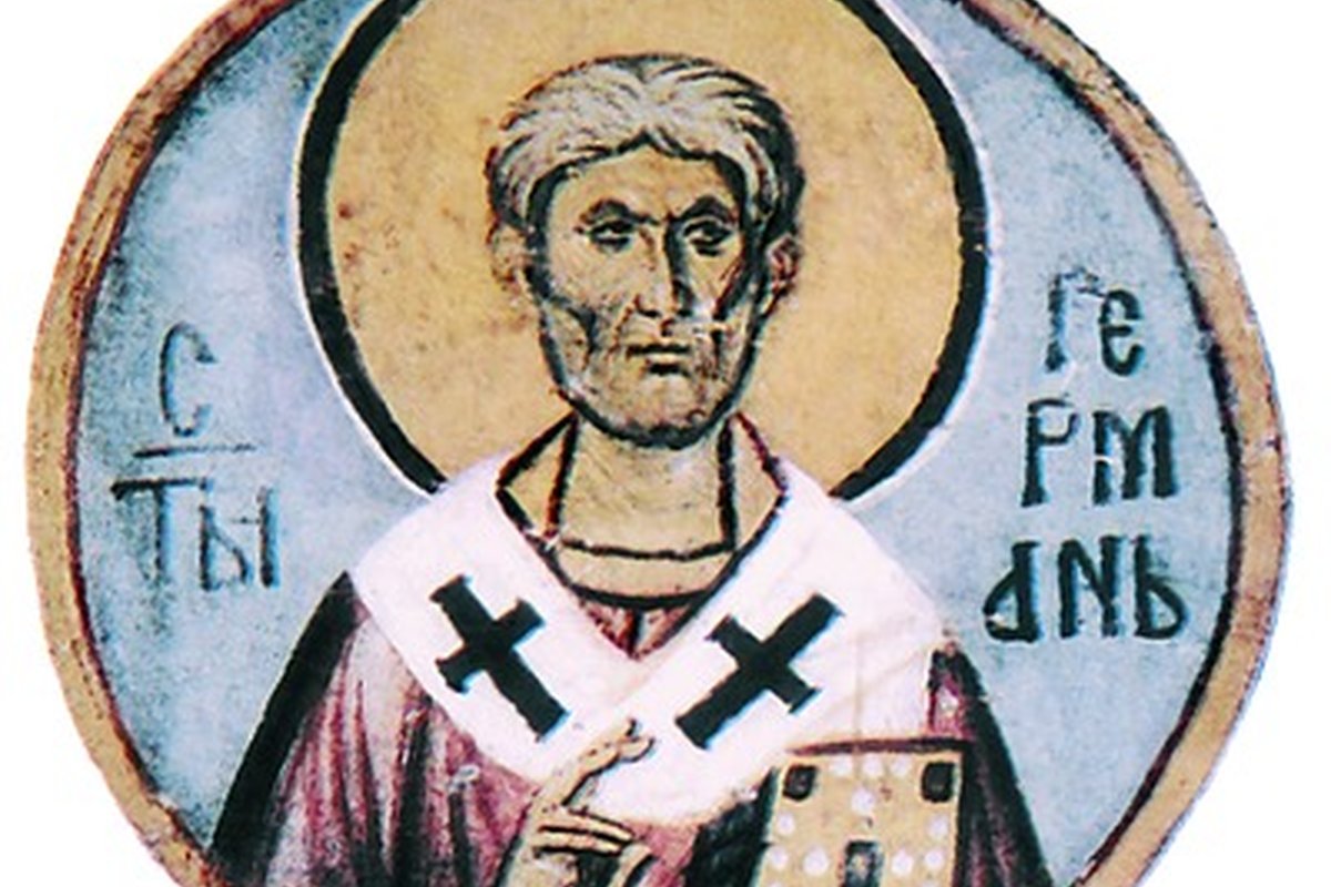 A medieval fresco roundel of a bearded bishop saint with a gold halo, wearing white clergy vestments marked with dark crosses, identified by a Cyrillic inscription as Germanus.