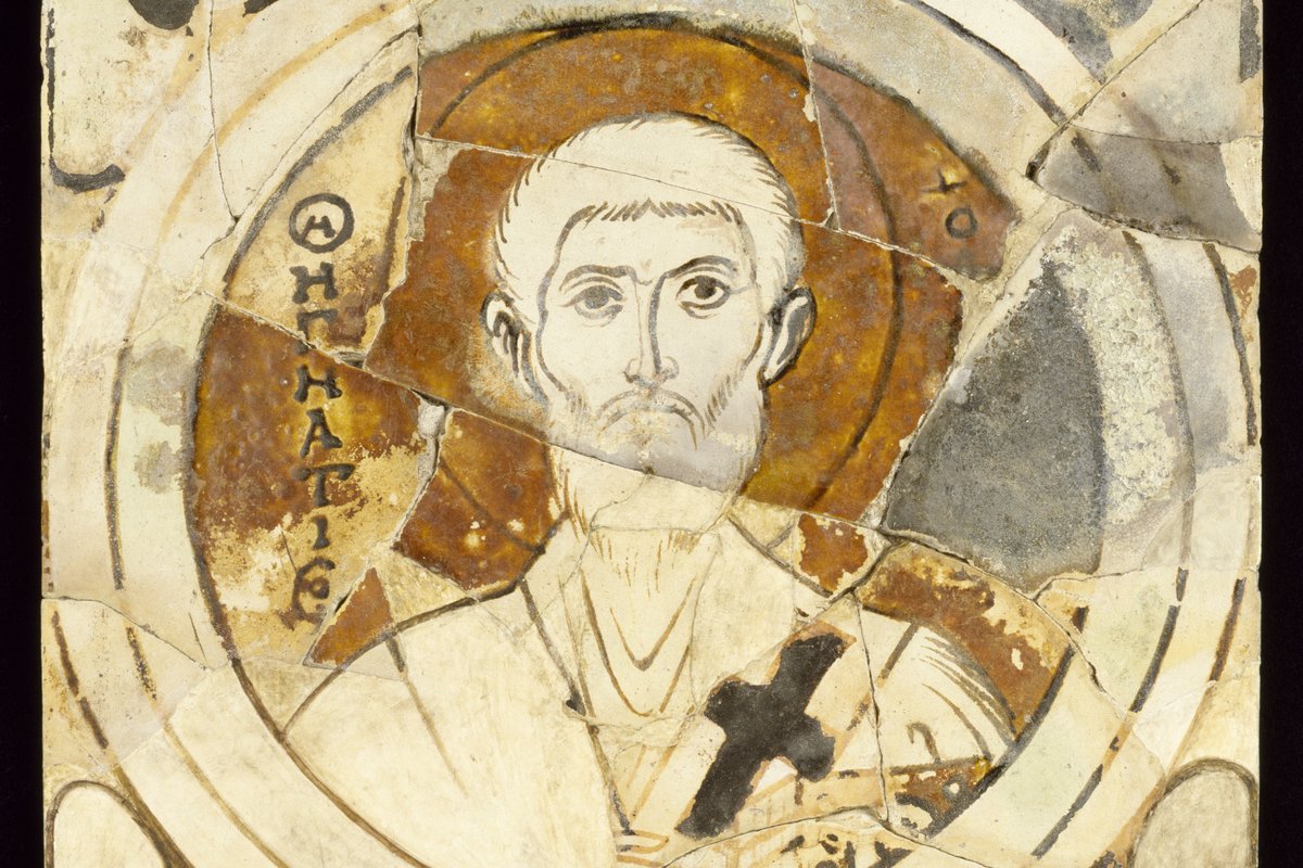 A fragmentary Byzantine icon of an elderly bearded bishop with a halo, holding a small cross, his name inscribed in Greek beside him.