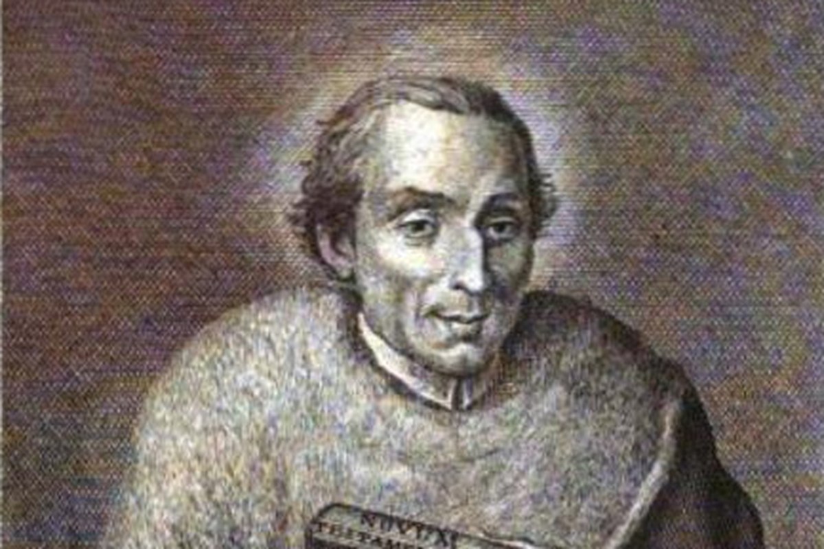 A portrait of a Roman Catholic priest in dark clerical vestments with a white collar, hands folded, gazing gently forward.
