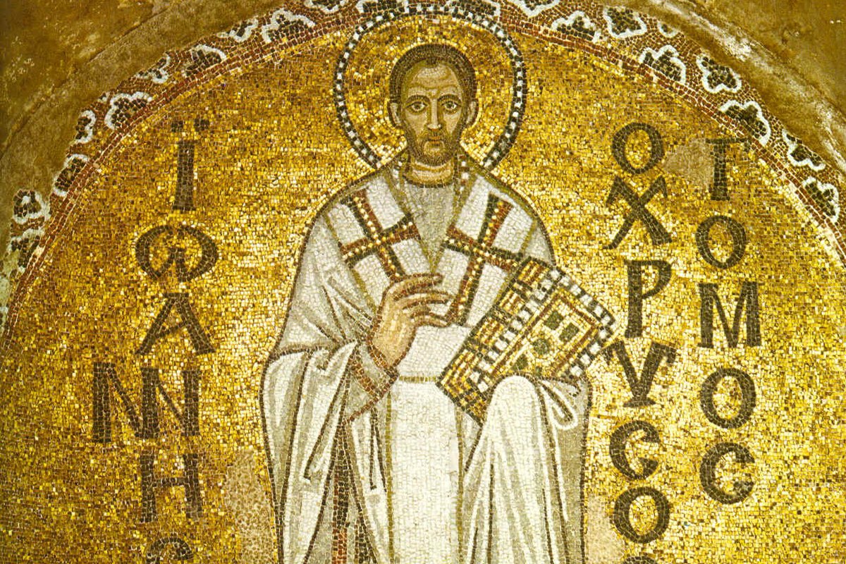 A golden Byzantine mosaic of a bearded bishop in white and gold vestments holding a jeweled book, framed by a halo and Greek inscriptions naming him John Chrysostom.
