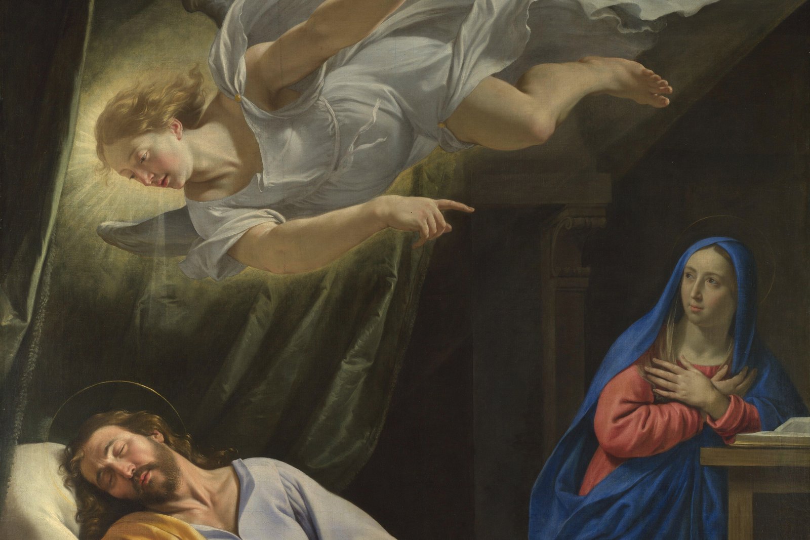 Joseph asleep in a chair beside a table, with a winged angel descending toward him in soft light, in a seventeenth-century French painting.