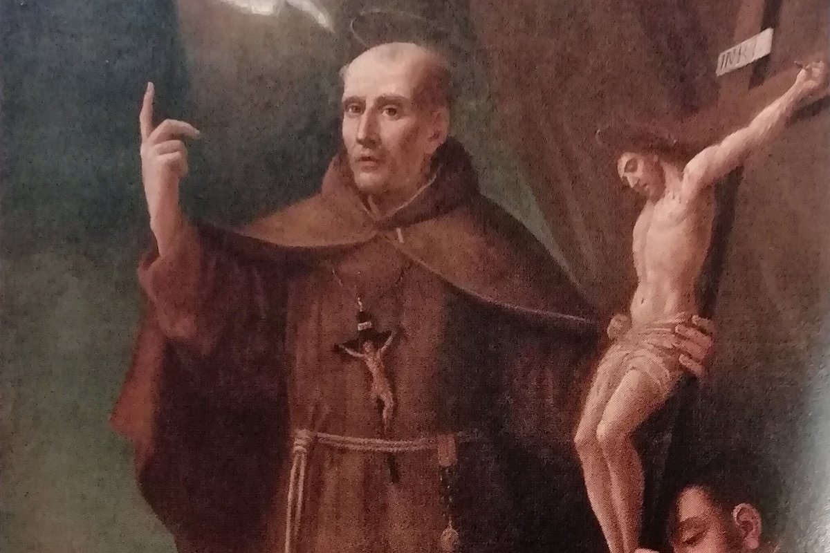 A Baroque portrait of a Franciscan friar in a brown habit, pointing upward with one hand, standing beside a crucifix and a skull resting on a table.