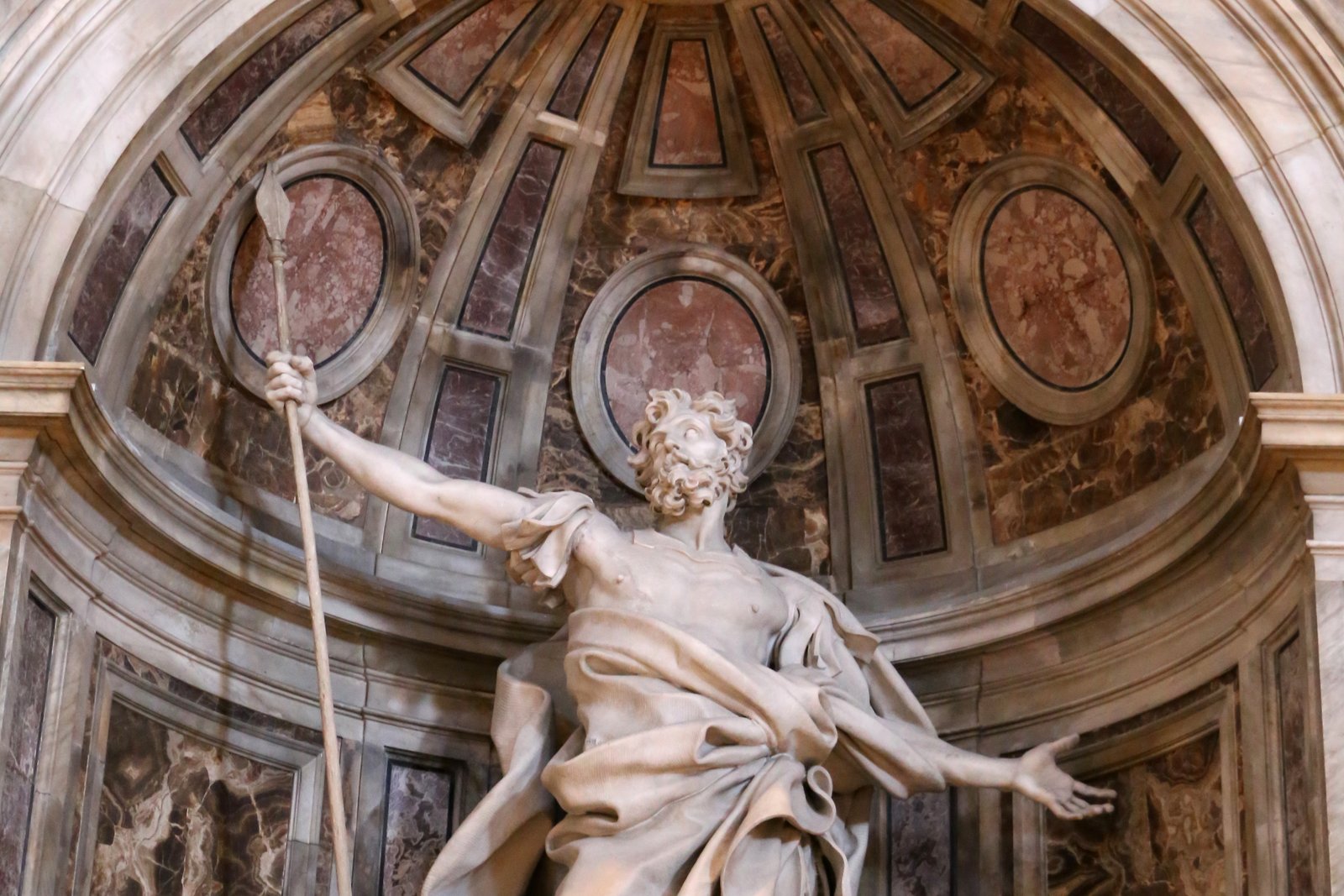 A marble statue of Saint Longinus by Gian Lorenzo Bernini, showing a bearded Roman soldier in flowing robes gazing upward with arms outstretched, one hand holding a long spear.