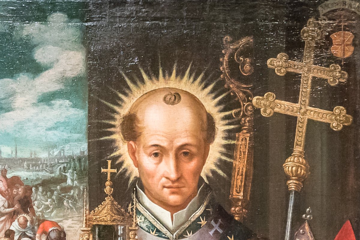 A haloed, tonsured archbishop in white and gold vestments stands beside a gold processional cross and monstrance, with a battle scene painted in the background.