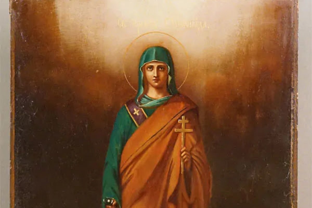 A devotional icon of a haloed woman in green and orange robes holding a small gold cross.