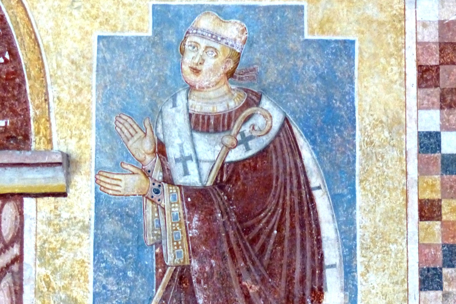 A weathered Romanesque fresco fragment showing a bishop saint in vestments, painted in earthy medieval pigments.