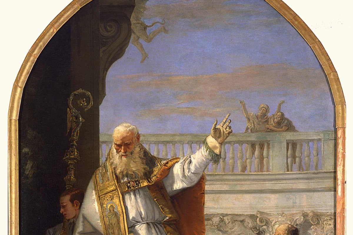 An elderly bishop in gold and white vestments raises his hand in blessing beneath an arched niche, holding a crosier, as onlookers watch from a balcony below.