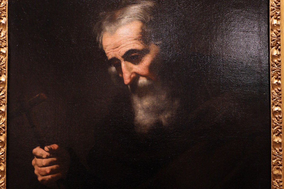 A dark, somber portrait of an elderly bearded man wrapped in a golden robe, looking down in quiet contemplation.