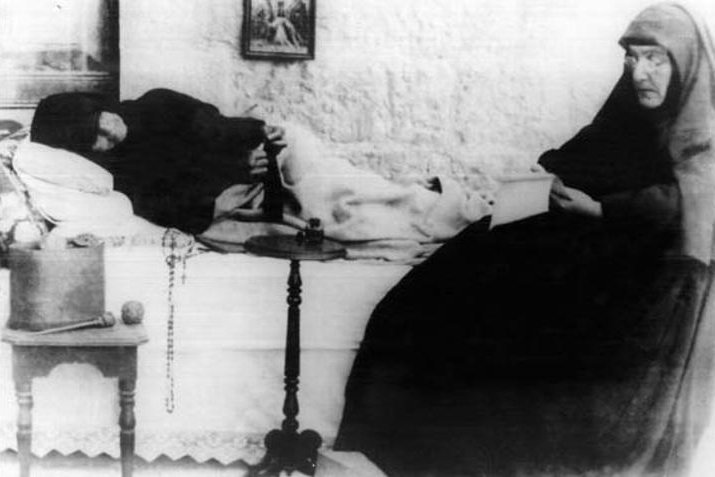 Una fotografía de época en blanco y negro de una monja maronita anciana con hábito oscuro y pañuelo en la cabeza, sentada con las manos juntas.