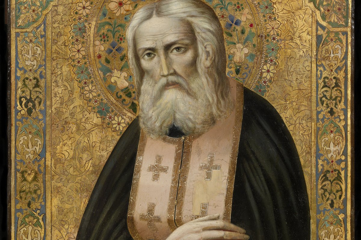 A gilded Russian Orthodox icon of Saint Seraphim of Sarov, an elderly monk with a long white beard, wearing a dark habit and an embroidered stole marked with crosses, set against an ornate gold background.