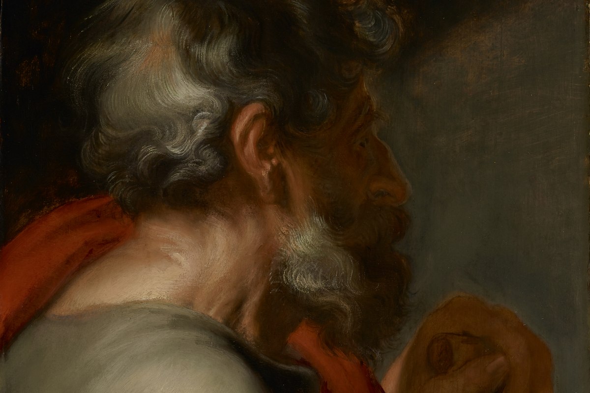 A close-up portrait of a bearded man in profile wearing a red cloak, gazing forward against a dark background.