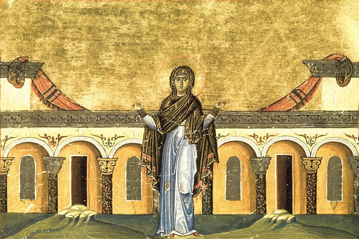 An 11th-century Byzantine illuminated manuscript miniature showing a haloed woman in dark monastic robes standing with raised hands before a colonnaded building, gold background.