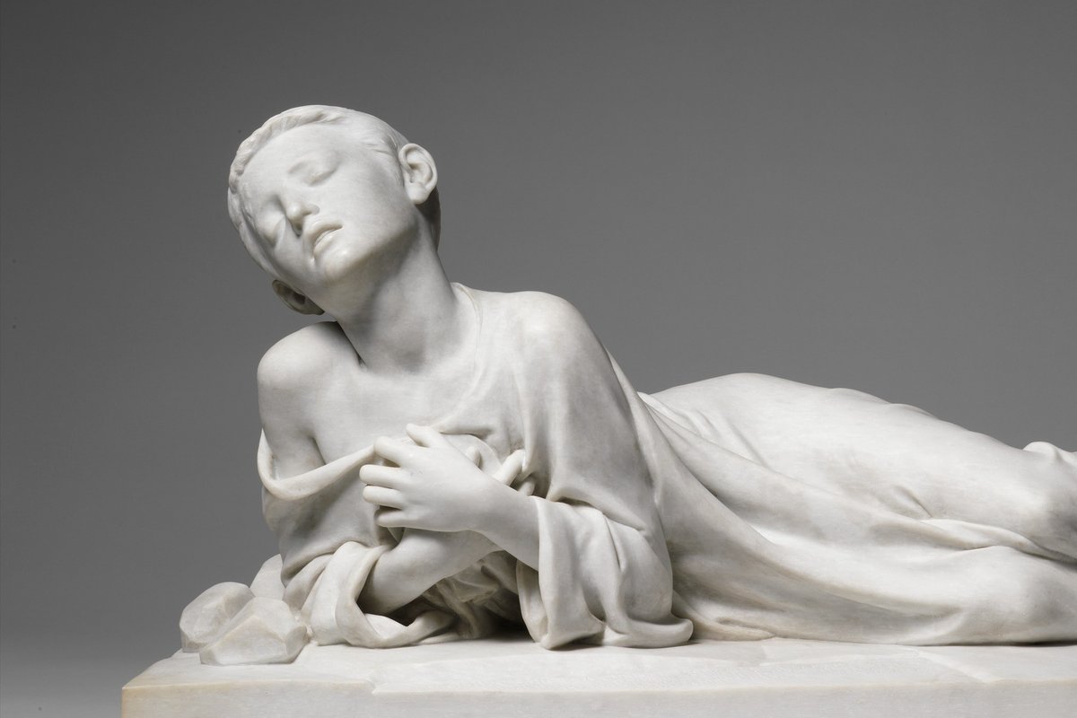 A white marble sculpture of the young martyr Saint Tarcisius lying fatally wounded, eyes closed, clutching the hidden Eucharist to his chest.