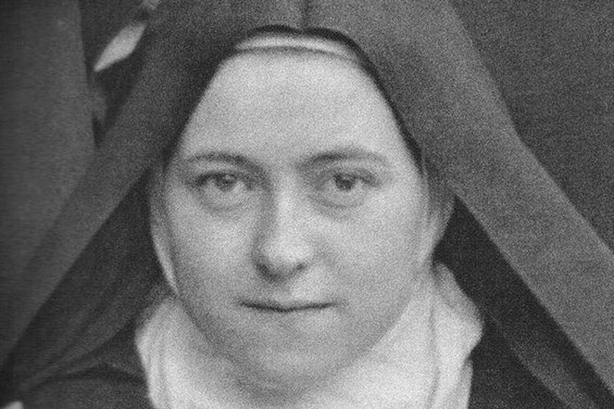 A close-up black-and-white photograph of a young Carmelite nun in a wimple and veil, gazing directly at the camera.
