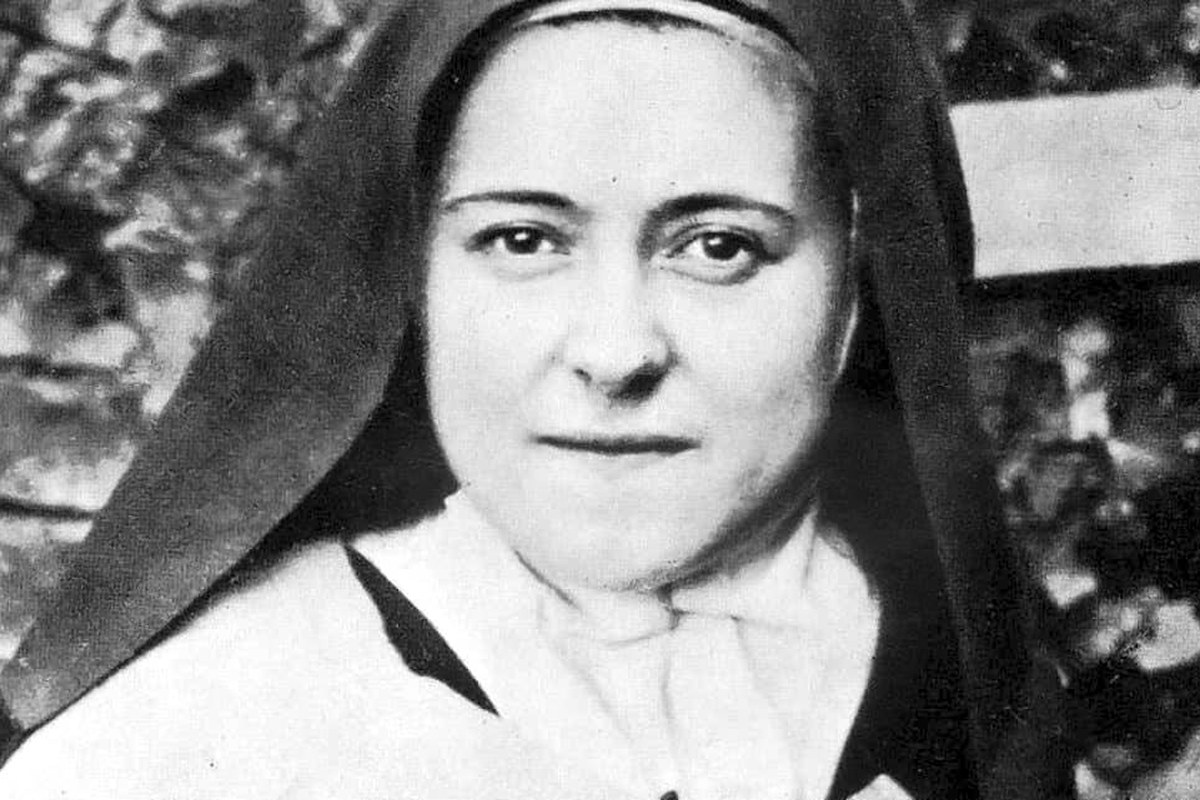 A black-and-white photograph of a young nun in a Carmelite habit, holding a crucifix and a bouquet of flowers.