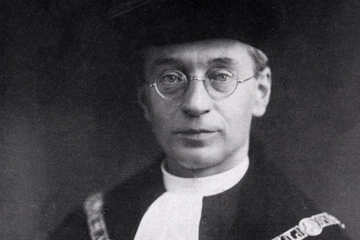 A black-and-white photograph of Titus Brandsma wearing round glasses and the academic robe and chain of office of rector magnificus of the Catholic University of Nijmegen.