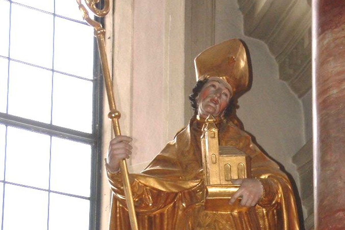A gilded statue of a bishop wearing a mitre and holding a crozier in one hand and a small model of a church in the other.