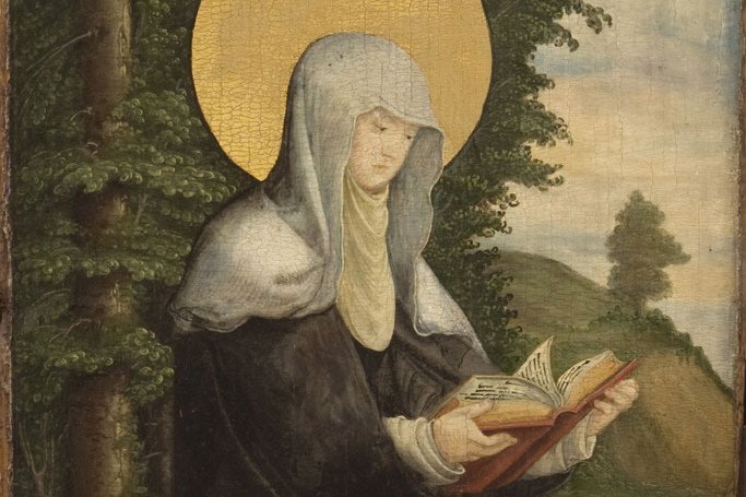 A tempera panel painting of Saint Walburga as a haloed Benedictine abbess in a dark habit and grey veil, reading from an open illuminated book, with a forest and abbey ruins in the background.