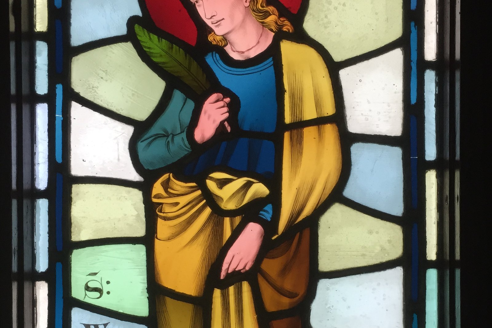 A stained glass window portrait of a young medieval woman saint in a blue robe, holding a martyr's palm, with a halo.