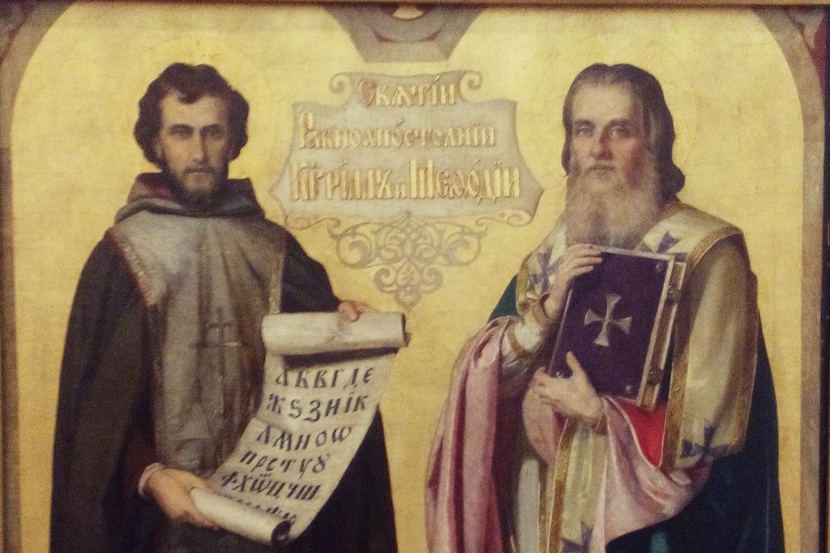 Two bearded Byzantine saints in ornate robes, one holding a scroll inscribed with an early Slavic alphabet, the other holding a jeweled Gospel book.