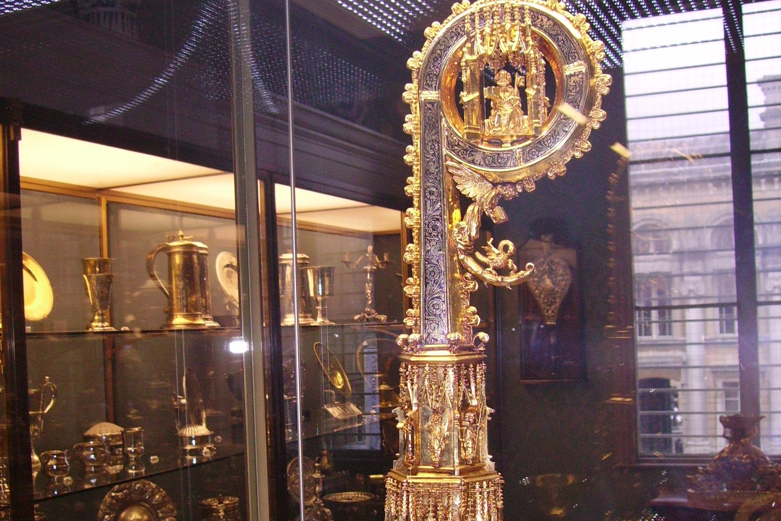 The ornate gilt silver crozier of Bishop Richard Fox, displayed in a museum case, showing its crooked head enclosing a small figure and its spiraling Gothic shaft