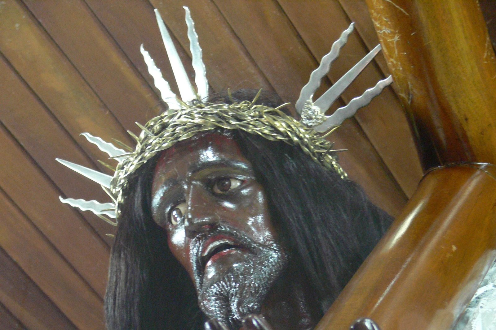 Close-up of the dark wooden face of the Black Christ statue, crowned with a crown of thorns and silver rays, carrying the wooden cross beam, inside the Church of San Felipe in Portobelo, Panama