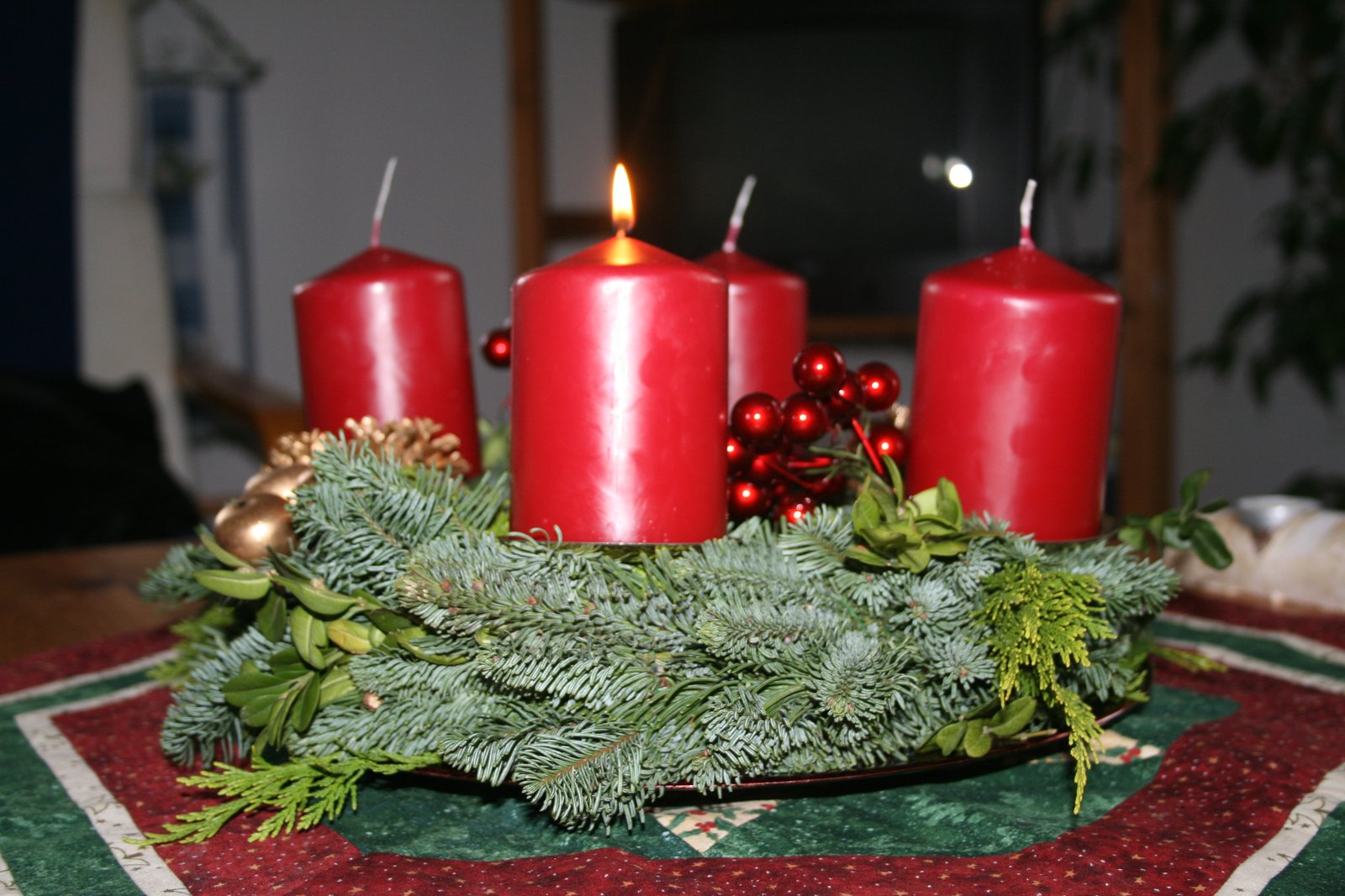 An Advent wreath with four red candles, one lit, surrounded by evergreen branches.