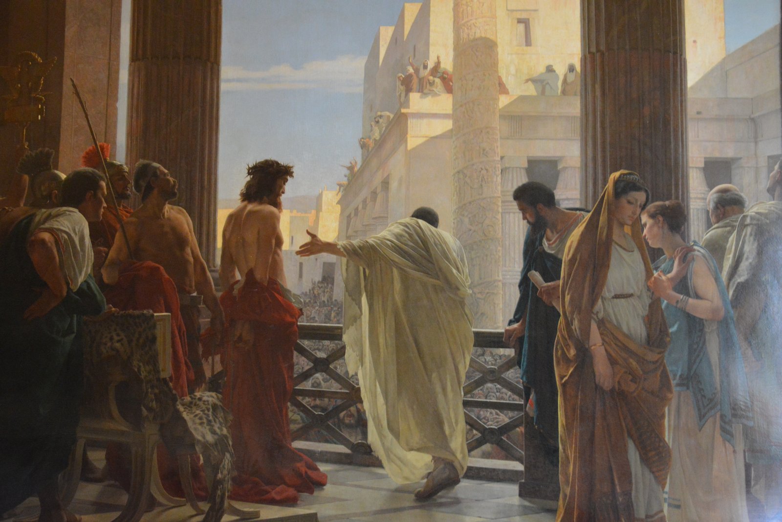 A 19th-century painting of Pontius Pilate presenting a bound, thorn-crowned Christ to a crowd from a balcony above a courtyard, seen from behind the two figures.