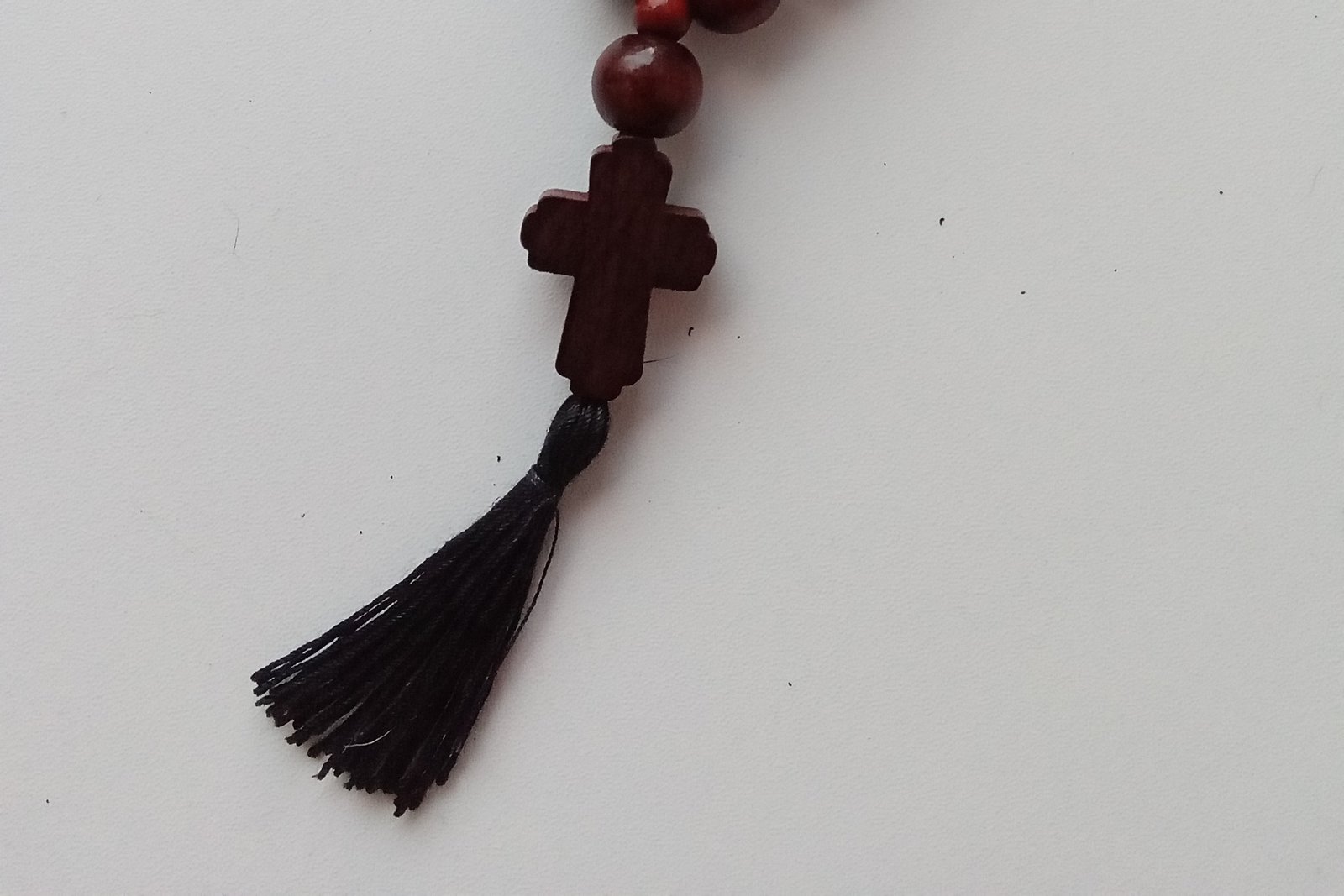 Fotografia en primer plano de un rosario de cuentas de madera enrollado sobre una superficie oscura, con un pequeño crucifijo visible al final.
