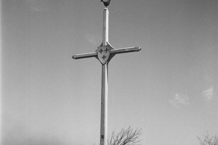 A tall wooden memorial cross marking the original site of Kateri Tekakwitha's tomb near Kahnawake, Quebec, photographed in 1947, before her remains were later moved into the St. Francis Xavier Mission church