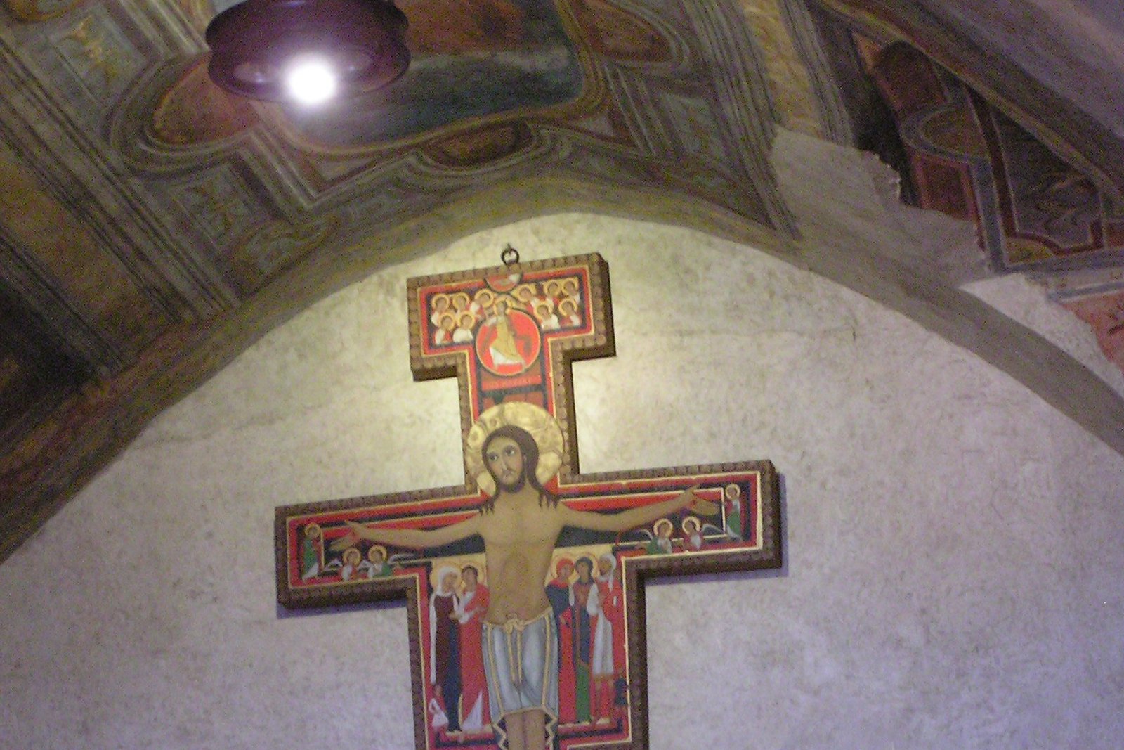 The San Damiano Cross, a painted Romanesque icon crucifix showing Christ standing upright with open eyes, surrounded by smaller figures of witnesses to the crucifixion and resurrection
