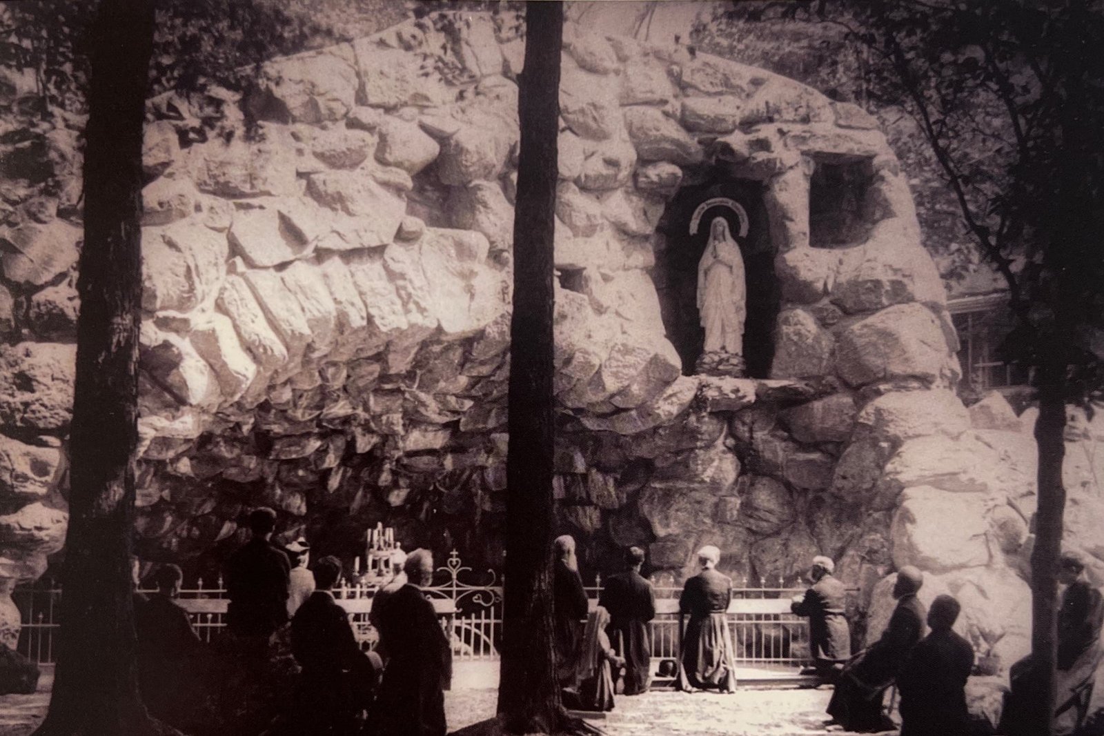 Historic 1896 black-and-white photograph of the Grotto of Massabielle at Lourdes, showing the rock niche and pilgrims gathered at the site of the spring