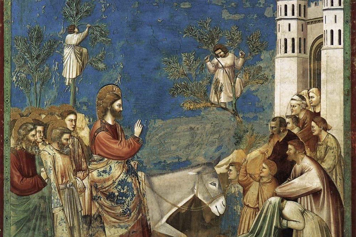 Giotto's fresco of Christ riding a donkey into Jerusalem as a crowd waves palm branches and lays cloaks on the ground before him, with a walled city gate to the right.